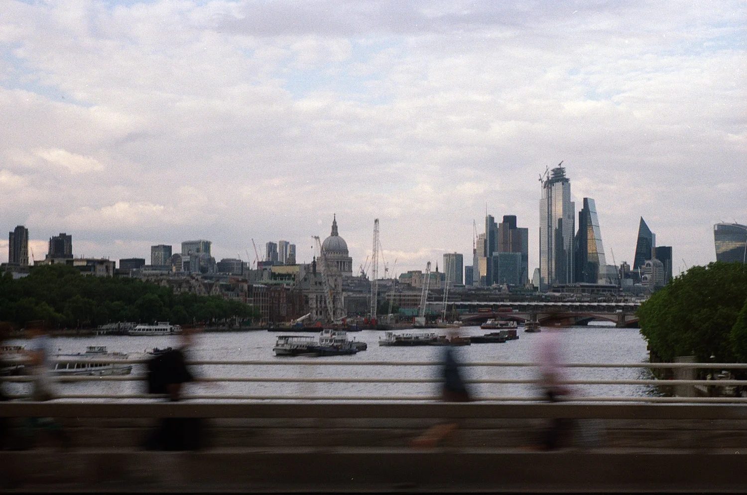 London skyline across the River Thames with St Paul's Cathedral and the City's towers, as blurred pedestrians cross a bridge in the foreground